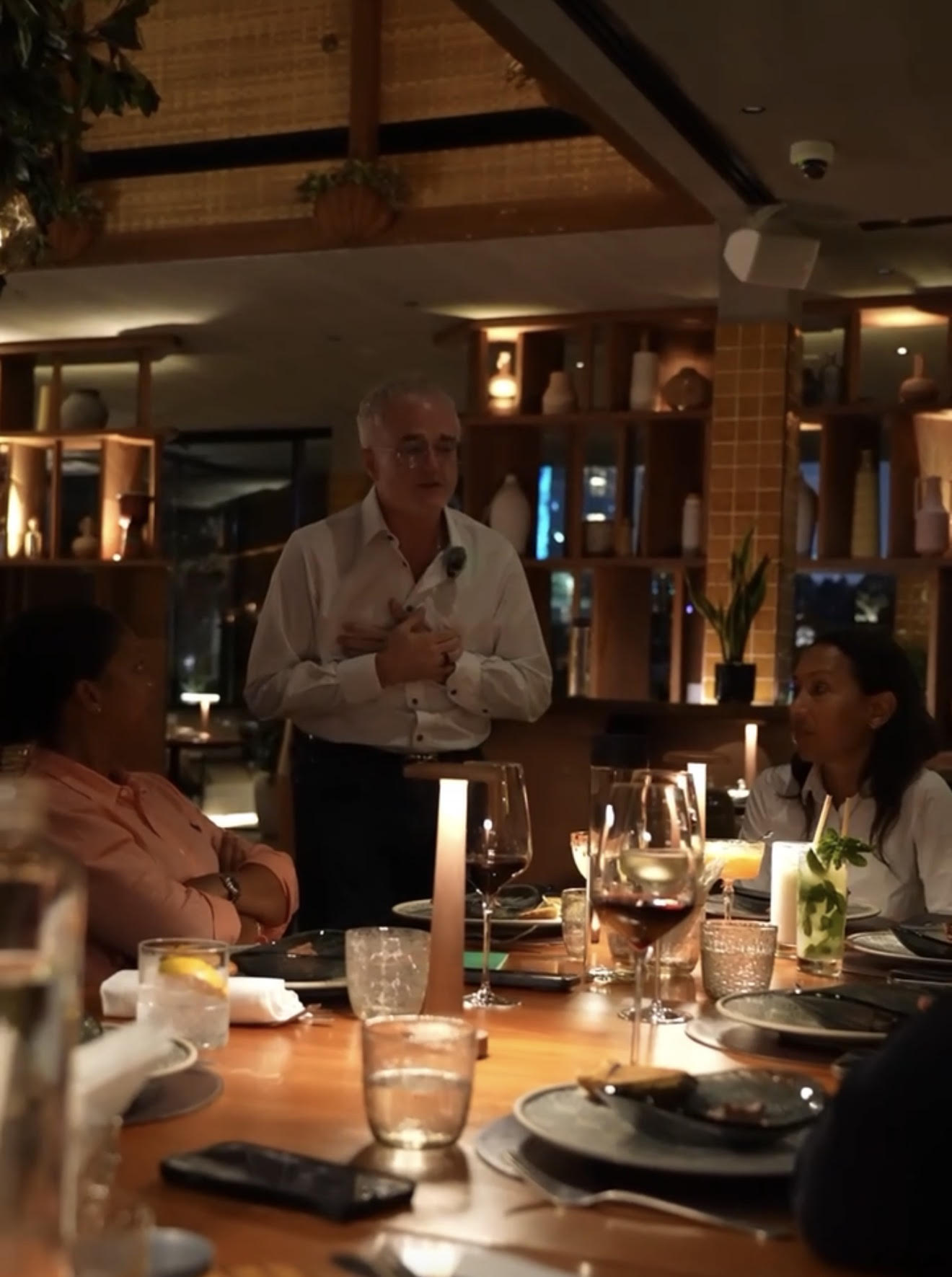 Dr. Jim Arnold leading a candlelit private dining-room conversation, warm golden lighting