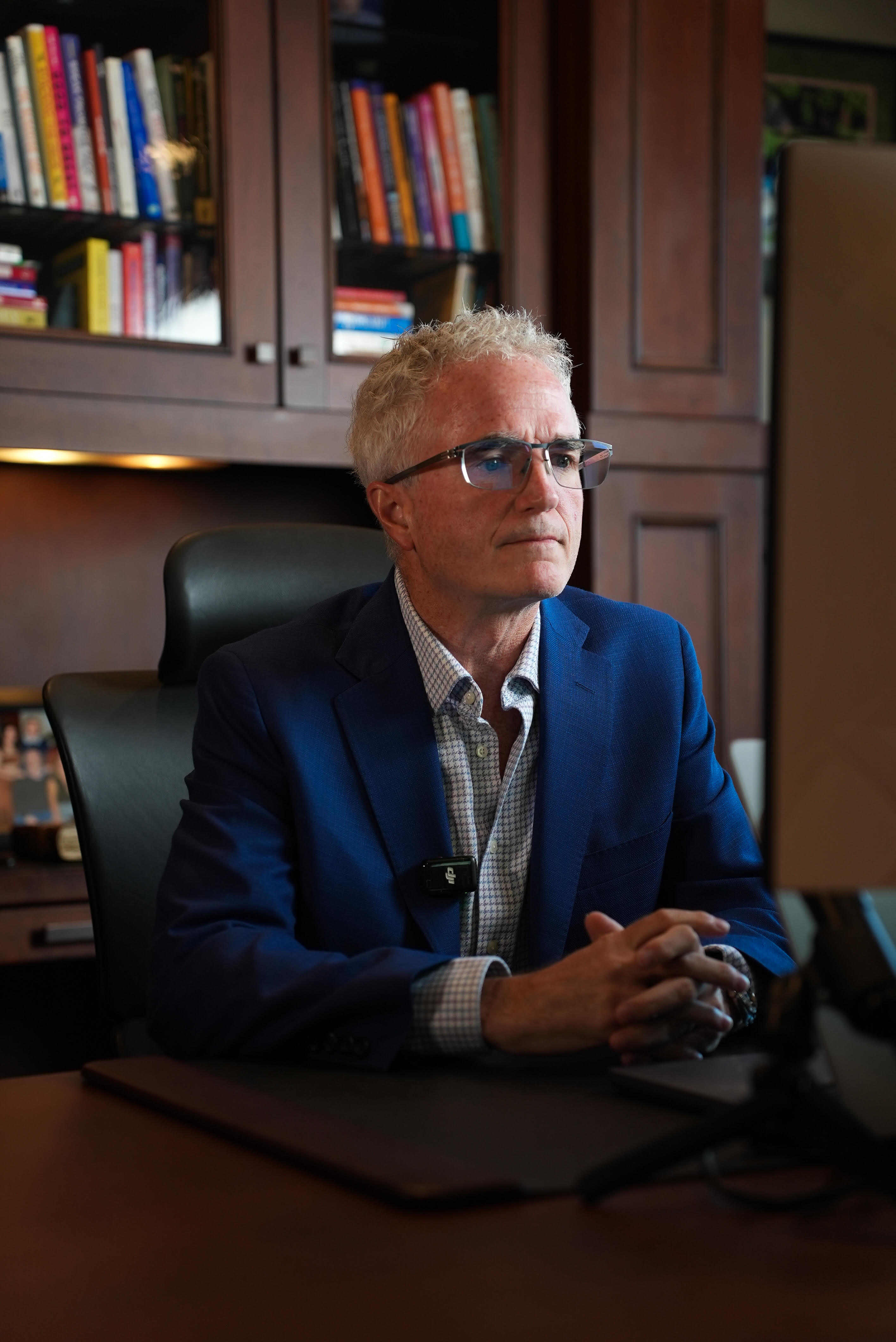 Dr. Jim Arnold at his desk, reflective, library bookcase in the background