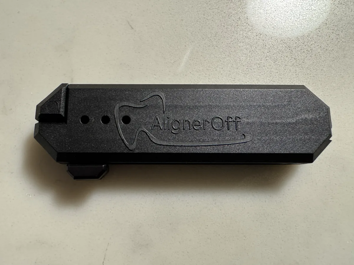 The AlignerOff device, a black moulded tool for removing clear aligners, resting on a countertop.