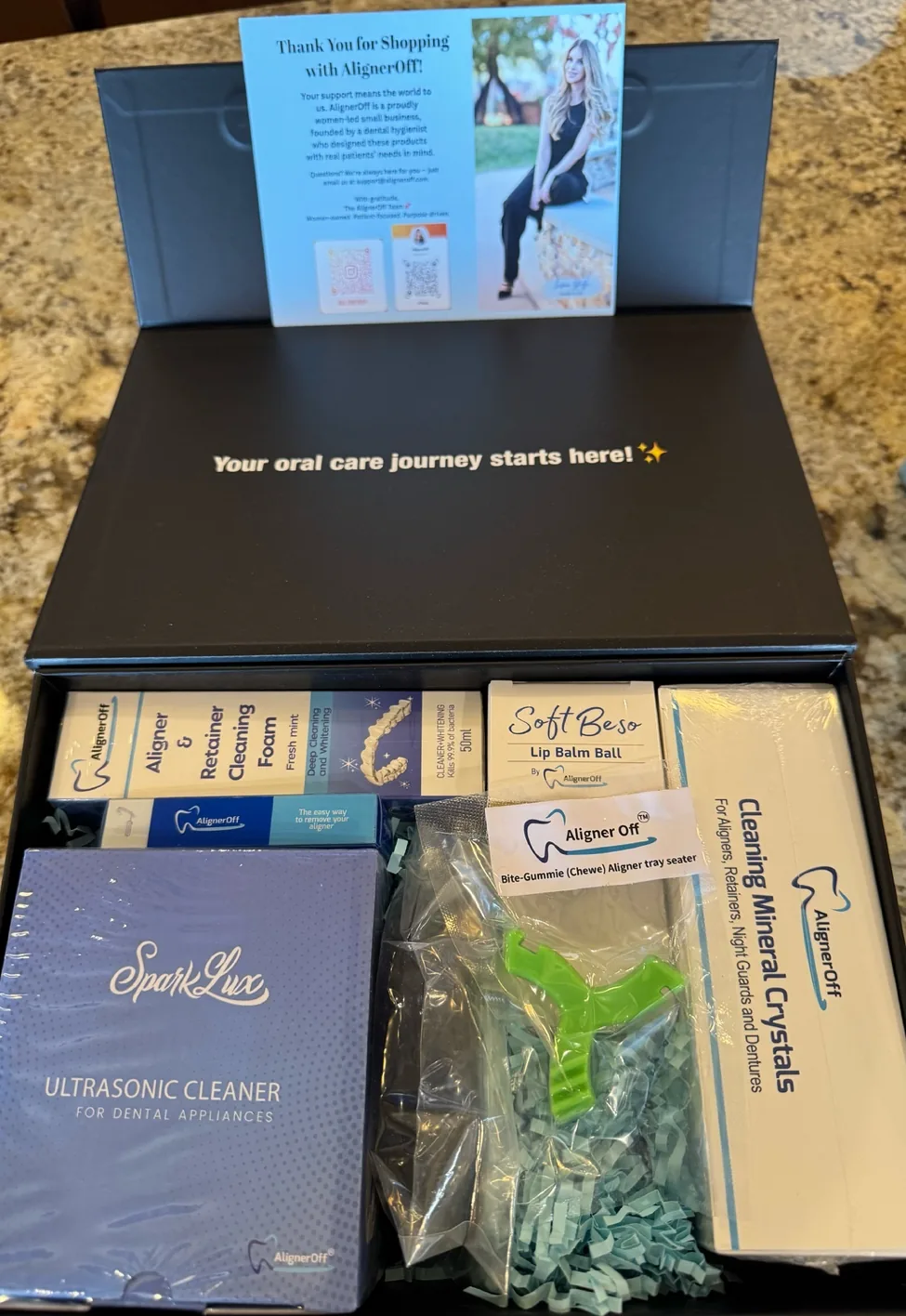 The contents of an AlignerOff oral care kit laid out, including an ultrasonic cleaner, mineral crystals and aligner accessories.