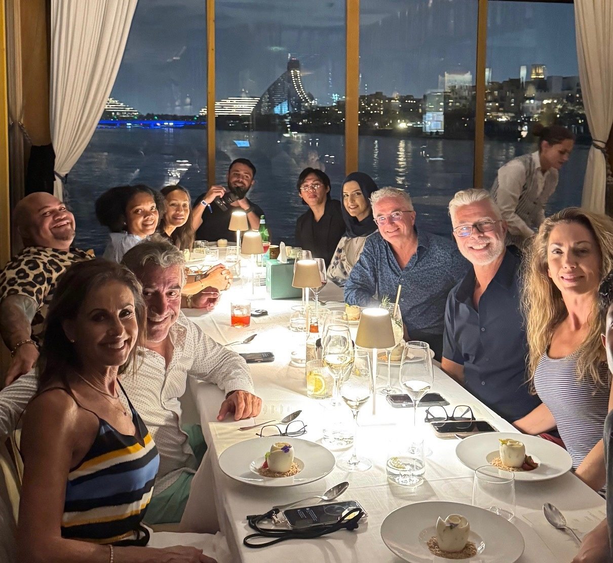The Dubai 2025 retreat group at a waterfront dinner with the Dubai skyline behind them
