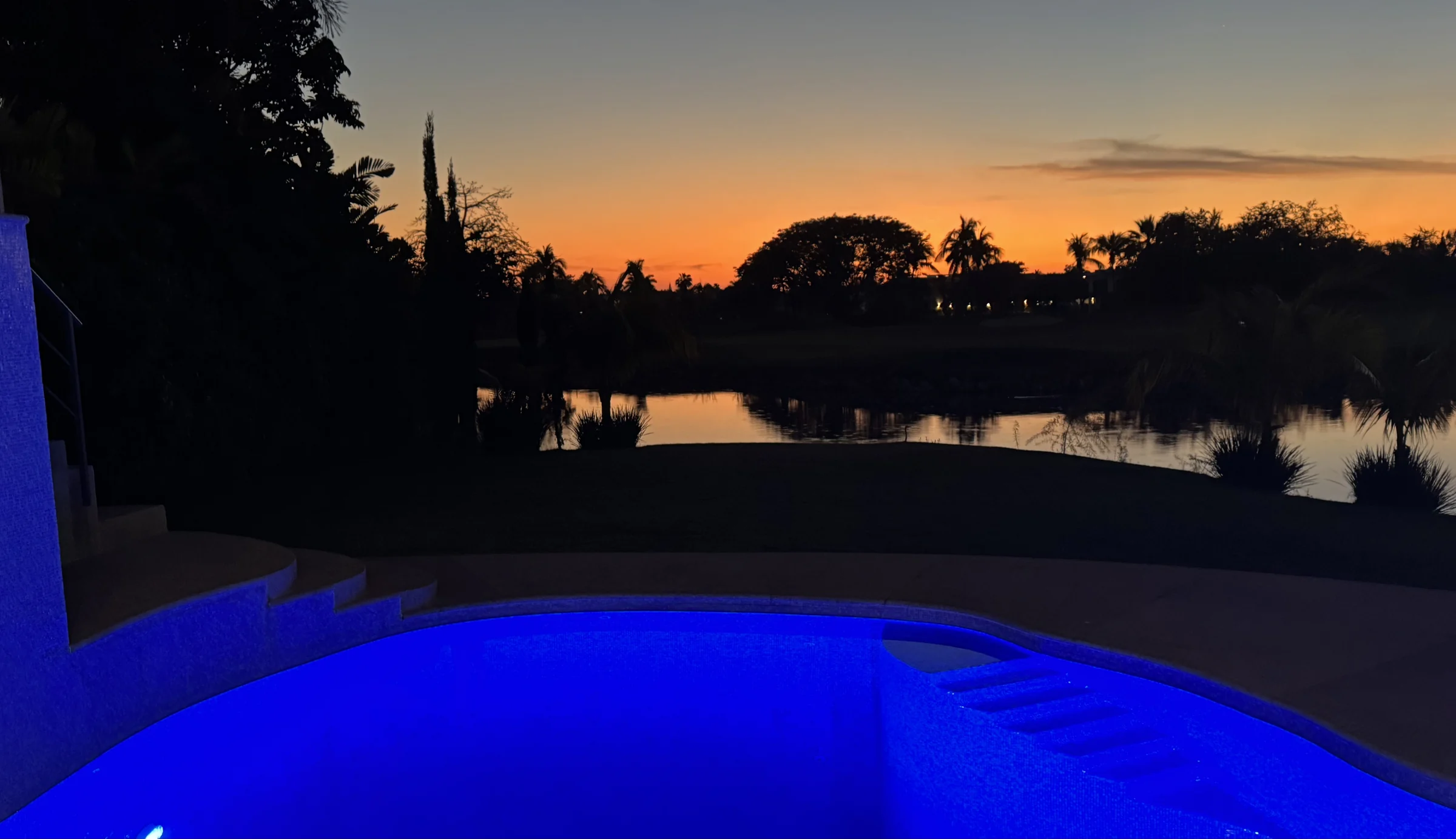 The illuminated pool against an orange sunset over the water